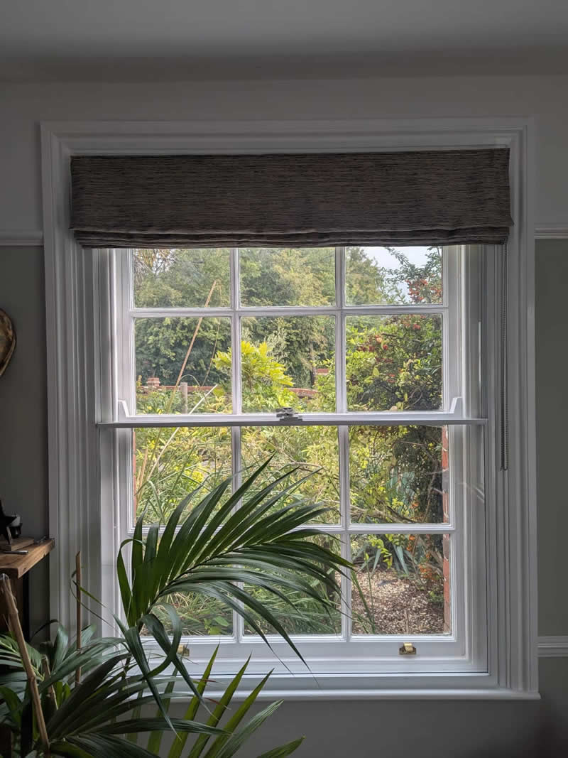 Window with secondary glazing, showcasing a view of a garden, featuring a decorative valance and indoor plants, emphasizing enhanced thermal efficiency and noise reduction benefits.