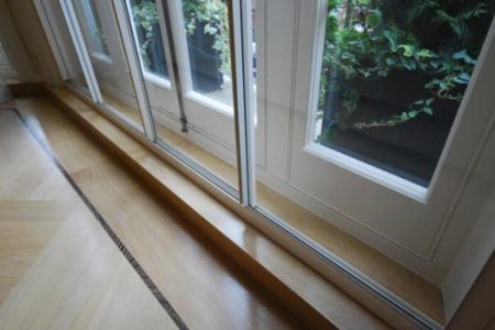 Four-panel slider secondary glazing unit installed in a bay window, showcasing wooden sill and greenery outside.