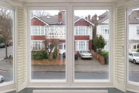 Bay window view featuring secondary glazing and external residential street scene with parked cars and greenery.