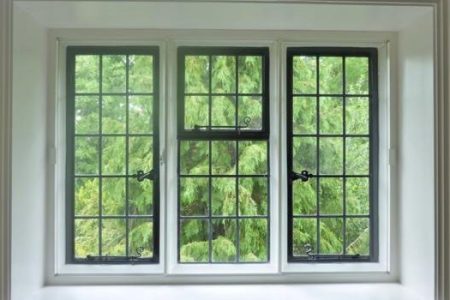 Three-panel bay window featuring black grid frames and a view of lush greenery outside, showcasing secondary glazing options for enhanced insulation.