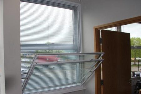 Tilt-in secondary glazing unit installed in a bay window, featuring integrated blinds, with a wooden door visible in the background.
